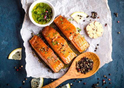 Delicious fried salmon fillet, seasonings on blue rustic concrete background. Cooked salmon steak with pepper, herbs, lemon, garlic, olive oil, spoon. Grilled fish. Fish for healthy dinner. Close-up